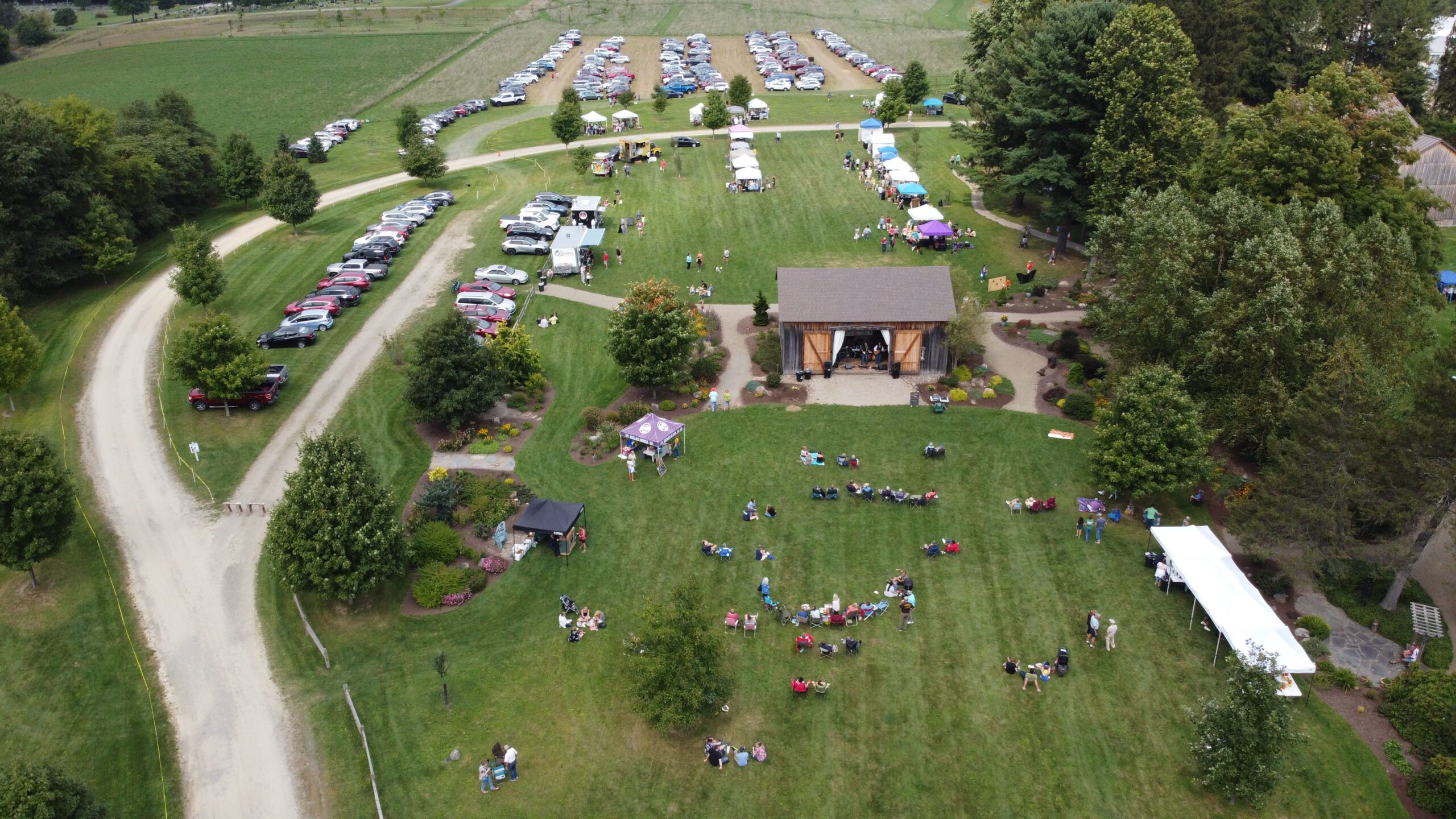 2021 Homegrown Harvest Festival Drone Photo: Taken from above, this photo shows the western grounds at Goodell Gardens & Homestead, including the Events Barn and southern Events Lawn. The lawns are filled with tents and people enjoying the festival. In the Background you can see the parking field.